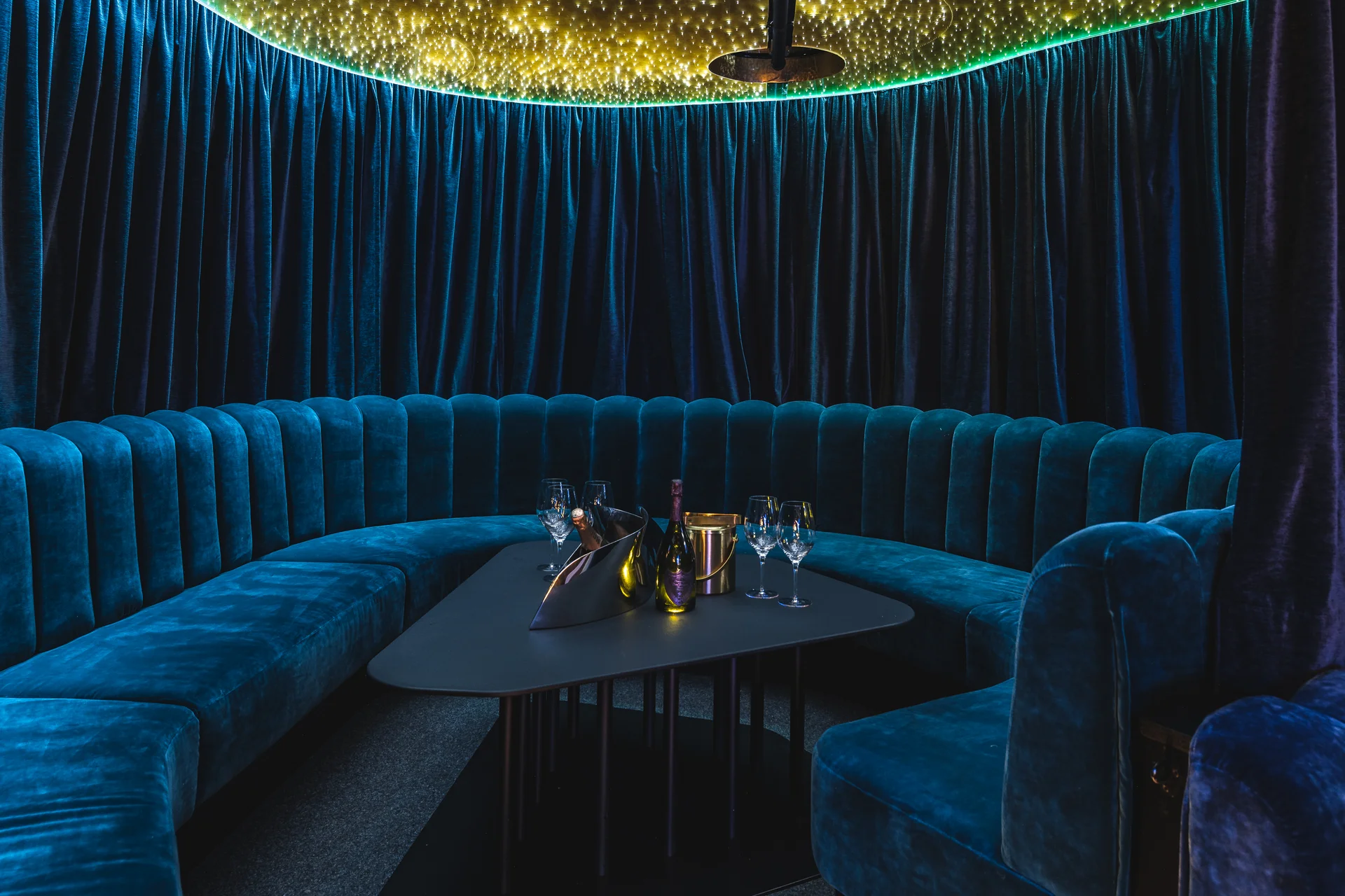 Rundsofa in blauem Samt mit gedecktem Tisch und Champagner-Setup unter einer Lichtinstallation im Club Luna Innsbruck.