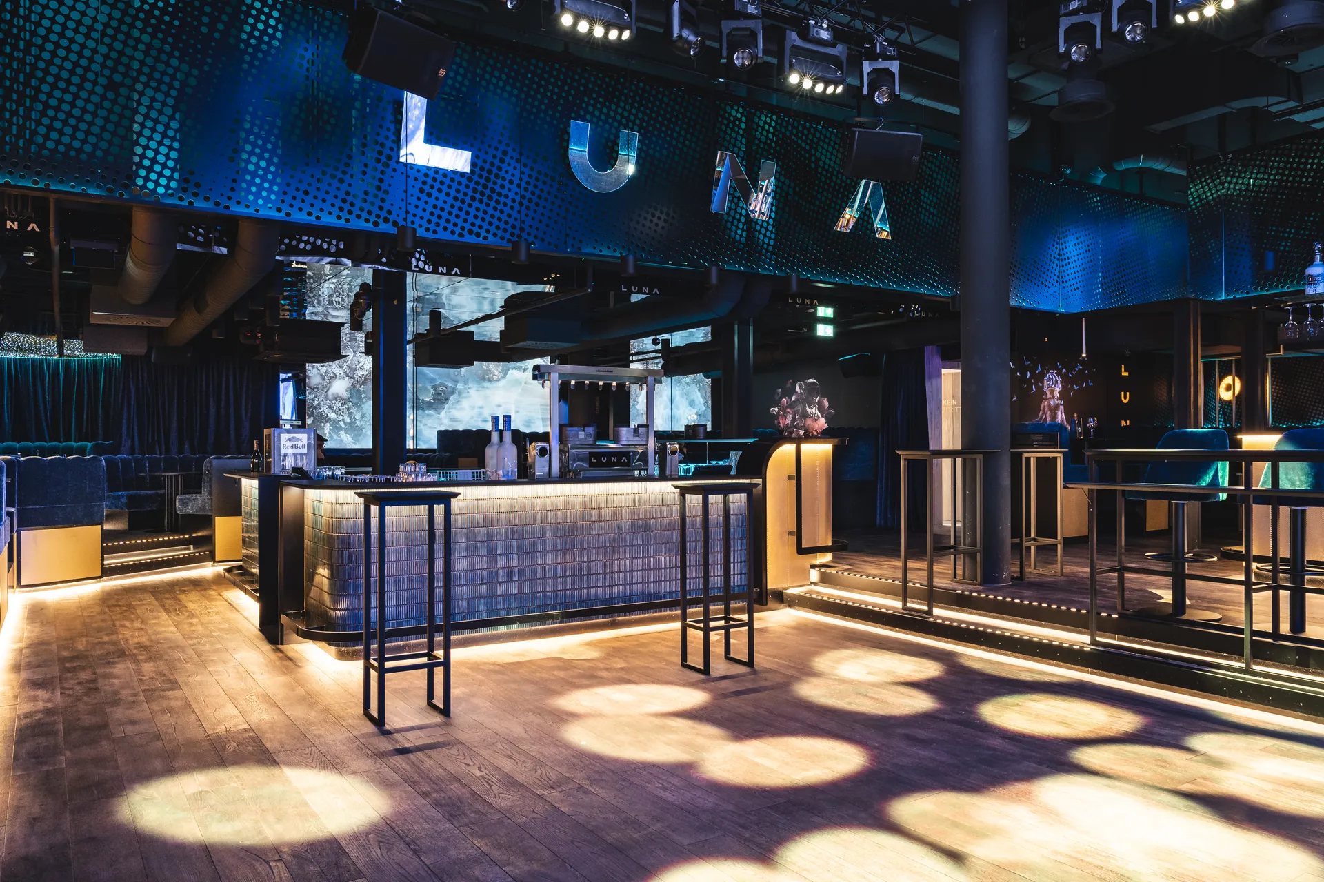 Blick auf Bar und leeren Dancefloor des Club Luna Innsbruck mit beleuchtetem LUNA-Schriftzug und Stehtischen.