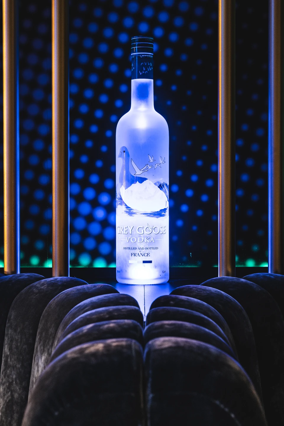 Beleuchtete Grey Goose Vodka-Flasche auf einem Samtsofa vor dem charakteristischen Lochblech-Hintergrund im Club Luna Innsbruck.