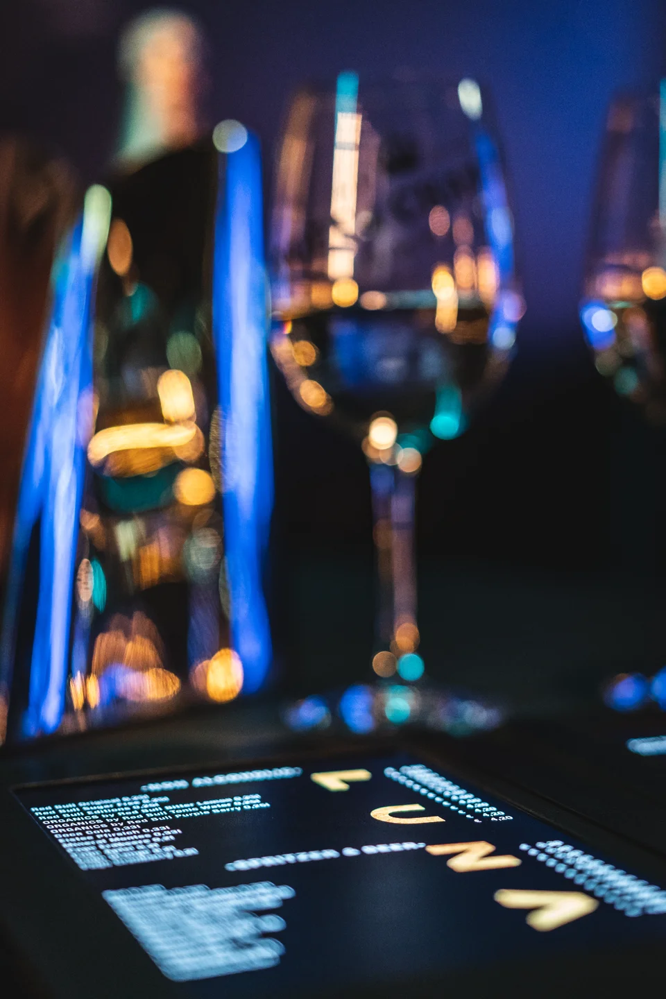 Beleuchtete Getränkekarte mit Weingläsern und farbigen Bokeh-Lichtpunkten im Club Luna Innsbruck.