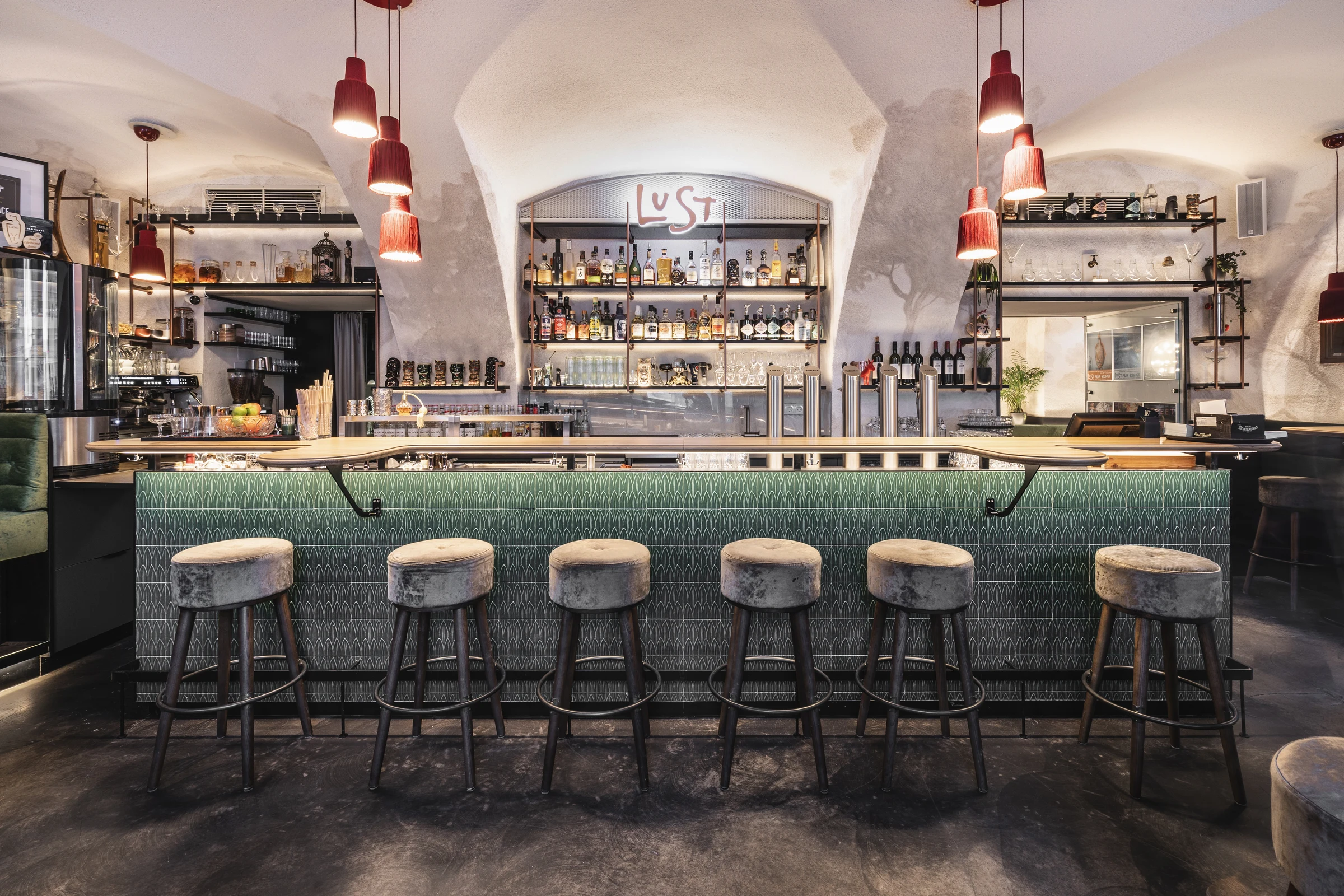 Bar des Lust in Bregenz mit grün gekacheltem Tresen, Samtbarhockern und gut bestückter Regalwand unter einem historischen Gewölbe.