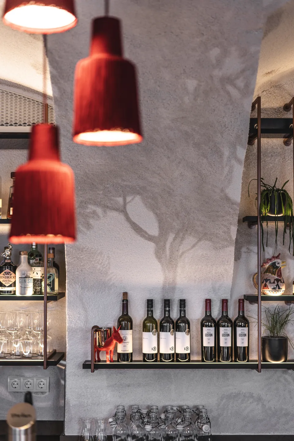Detailansicht des Weinregals im Lust Bregenz mit roten Pendelleuchten und einem aufgemalten Baummotiv auf dem Gewölbeputz.