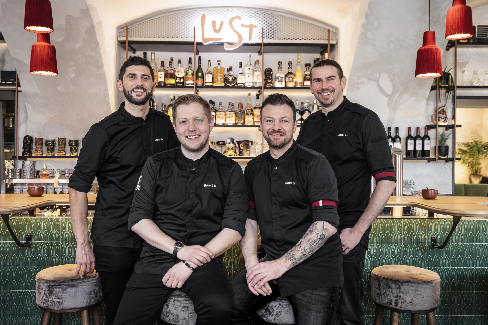 Das vierköpfige Team des Lust in Bregenz posiert lächelnd vor dem Bartresen mit beleuchtetem LUST-Schriftzug und gut bestückter Spirituosenregalwand.