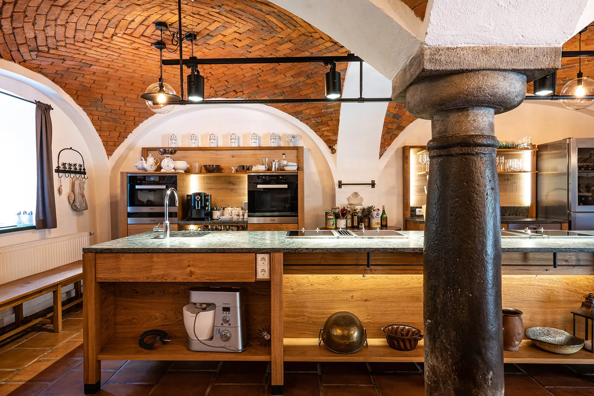 Historische Gewölbeküche im Gasthaus Maderthaner Weistrach mit Ziegelsteindecke, massiver Steinsäule, Kochinsel aus Holz mit Granitplatte und modernen Einbaugeräten.