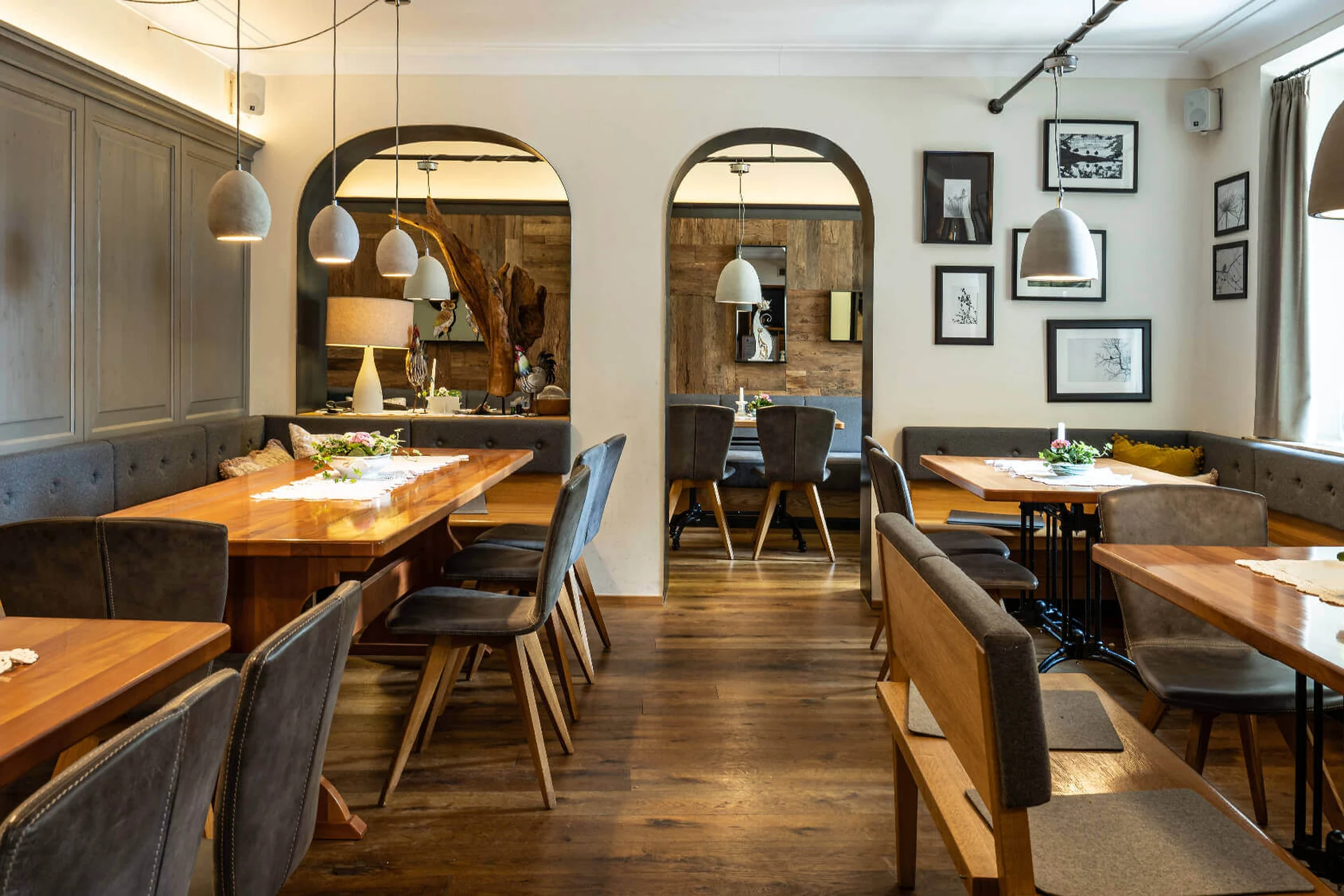 Gemütliche Gaststube im Gasthaus Maderthaner Weistrach mit langen Holztischen, grauen Sesseln, Sitzbänken, Bogendurchgängen und Wandbildern.