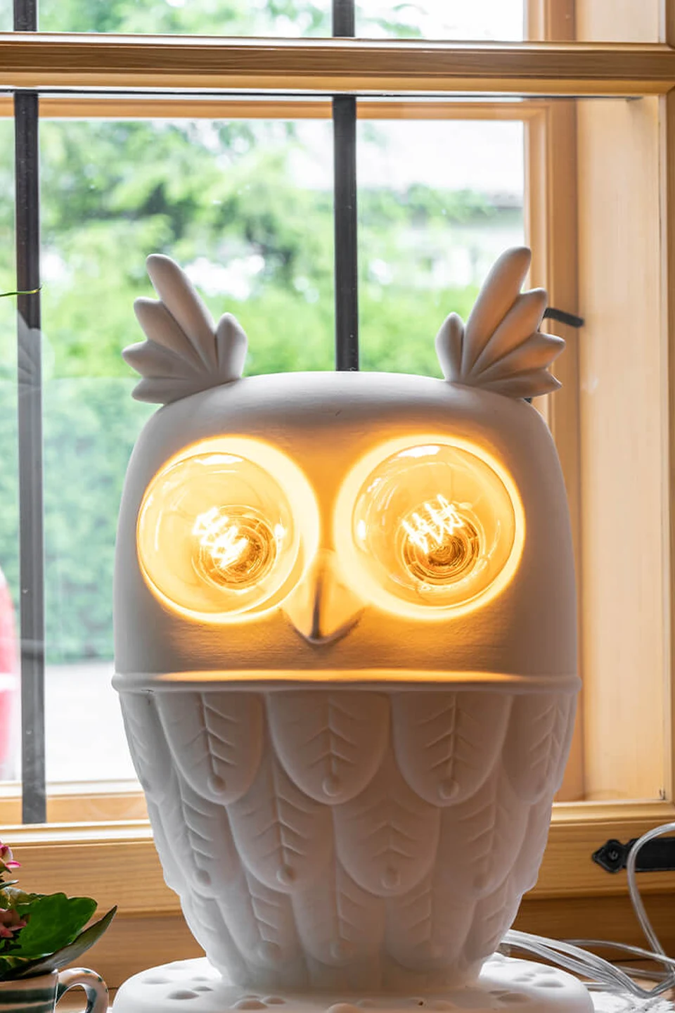 Leuchtende Eulen-Tischlampe aus weißer Keramik auf der Fensterbank im Gasthaus Maderthaner Weistrach mit Blick in den Garten.