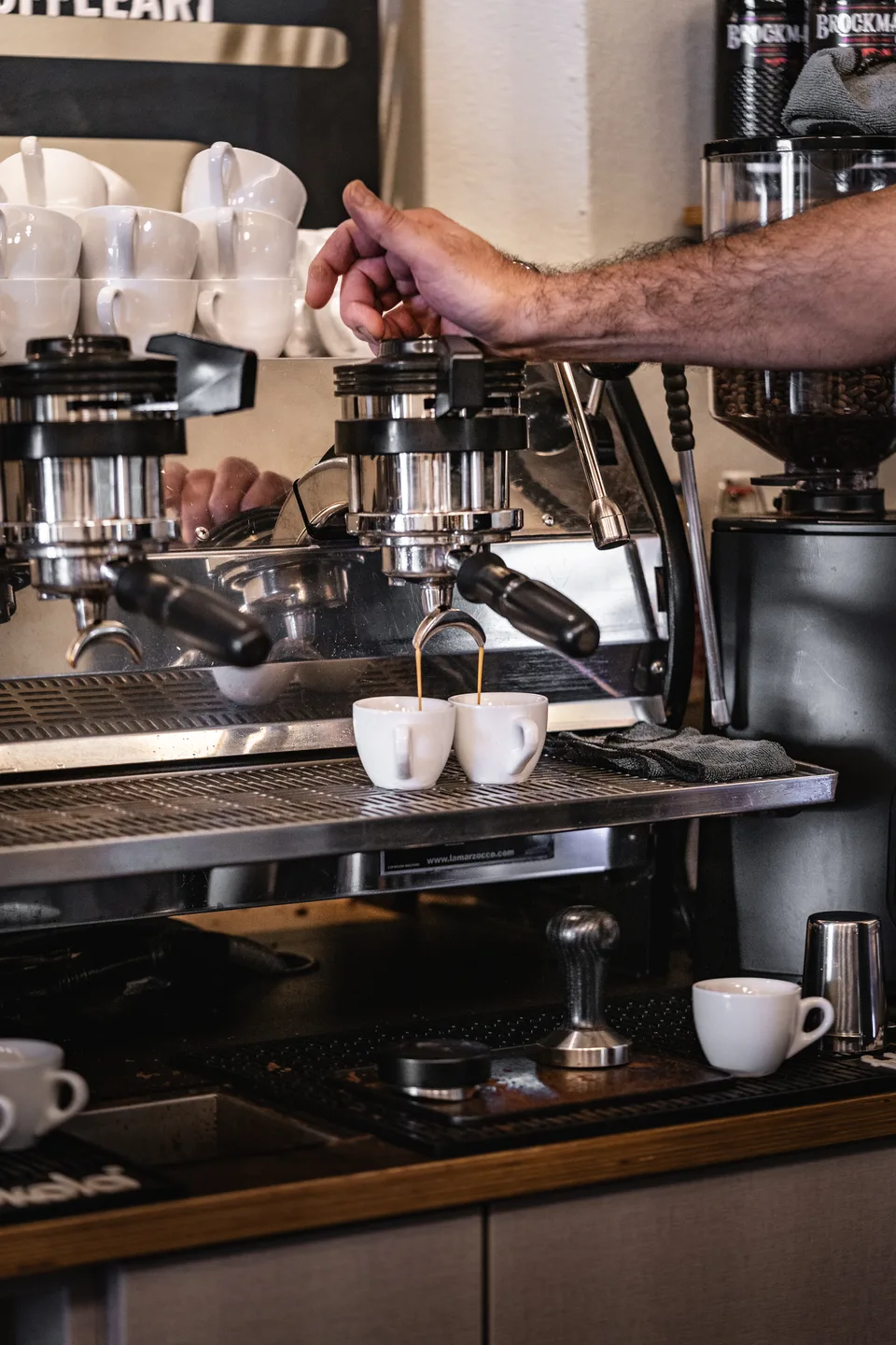 Barista lässt frischen Espresso in zwei weiße Tassen einer La Marzocco Siebträgermaschine im Café Momo Coffeeart in Feldkirch einlaufen.