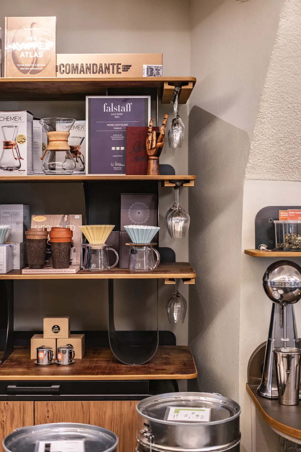 Regal im Café Momo Coffeeart in Feldkirch mit Chemex, V60-Drippern, Kaffeezubehör und einer Falstaff Café Guide Auszeichnung 2024.
