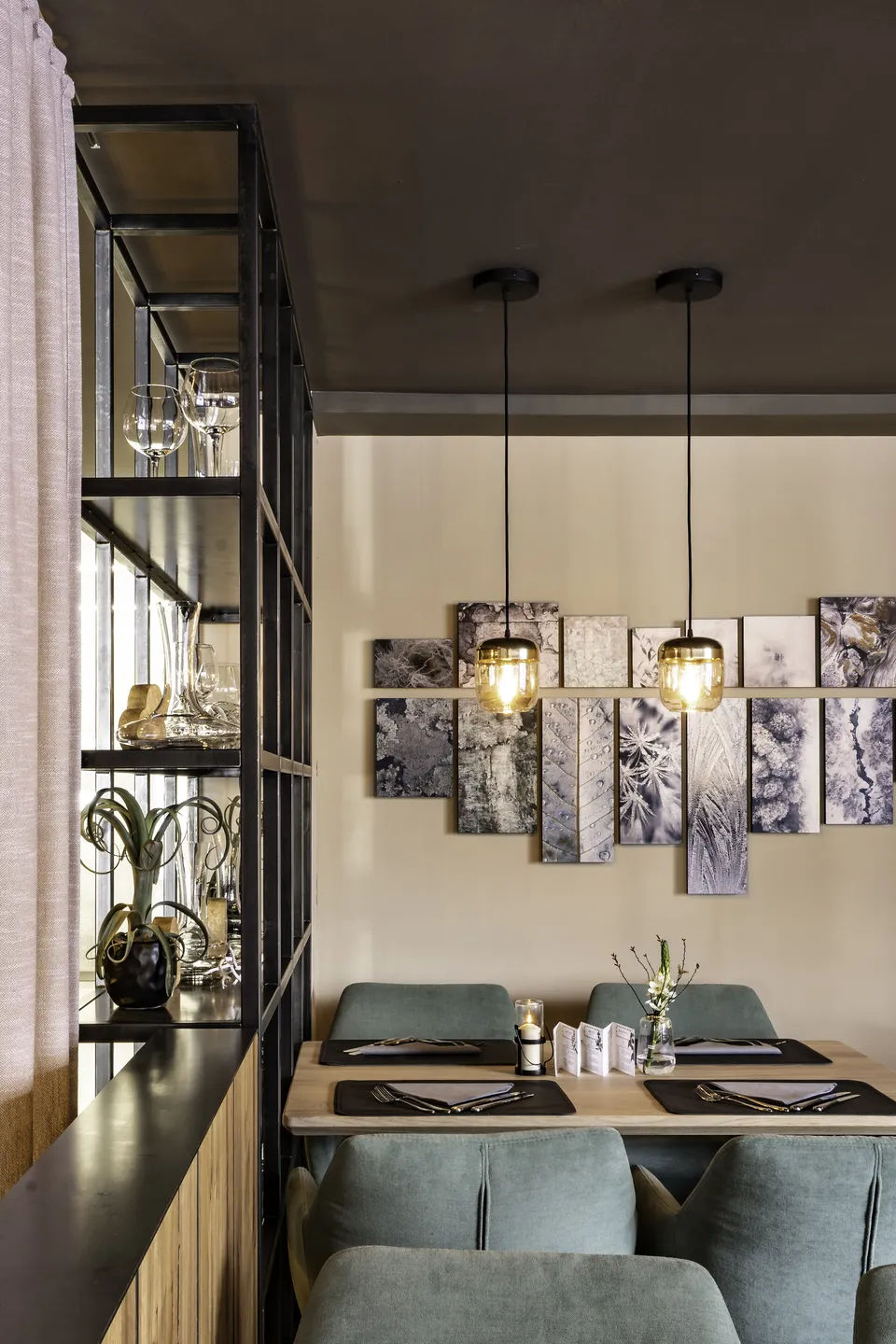 Sitzbereich im Restaurant Freestyle in Kaprun mit gedecktem Holztisch, mintgrünen Samtsesseln, goldenen Pendelleuchten und einer großen Fotocollage aus Naturmotiven an der Wand.