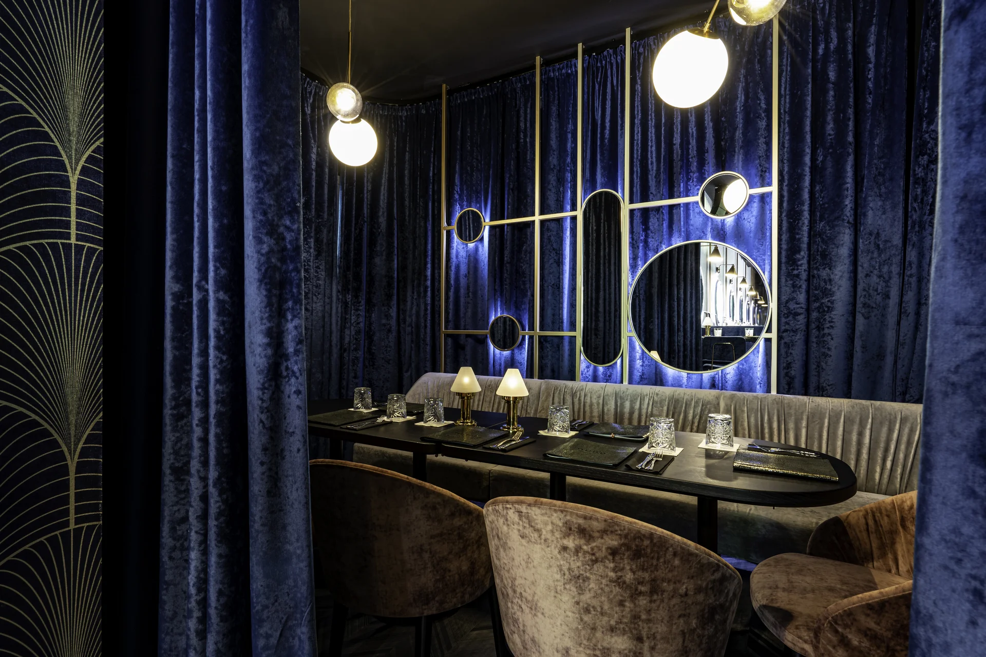 Privatbereich der Nuba Bar in Linz mit blauem Samtvorhang, gedecktem Tisch mit goldenen Tischlämpchen und Kristallgläsern sowie einem goldgerahmten Spiegelpaneel an der Rückwand.