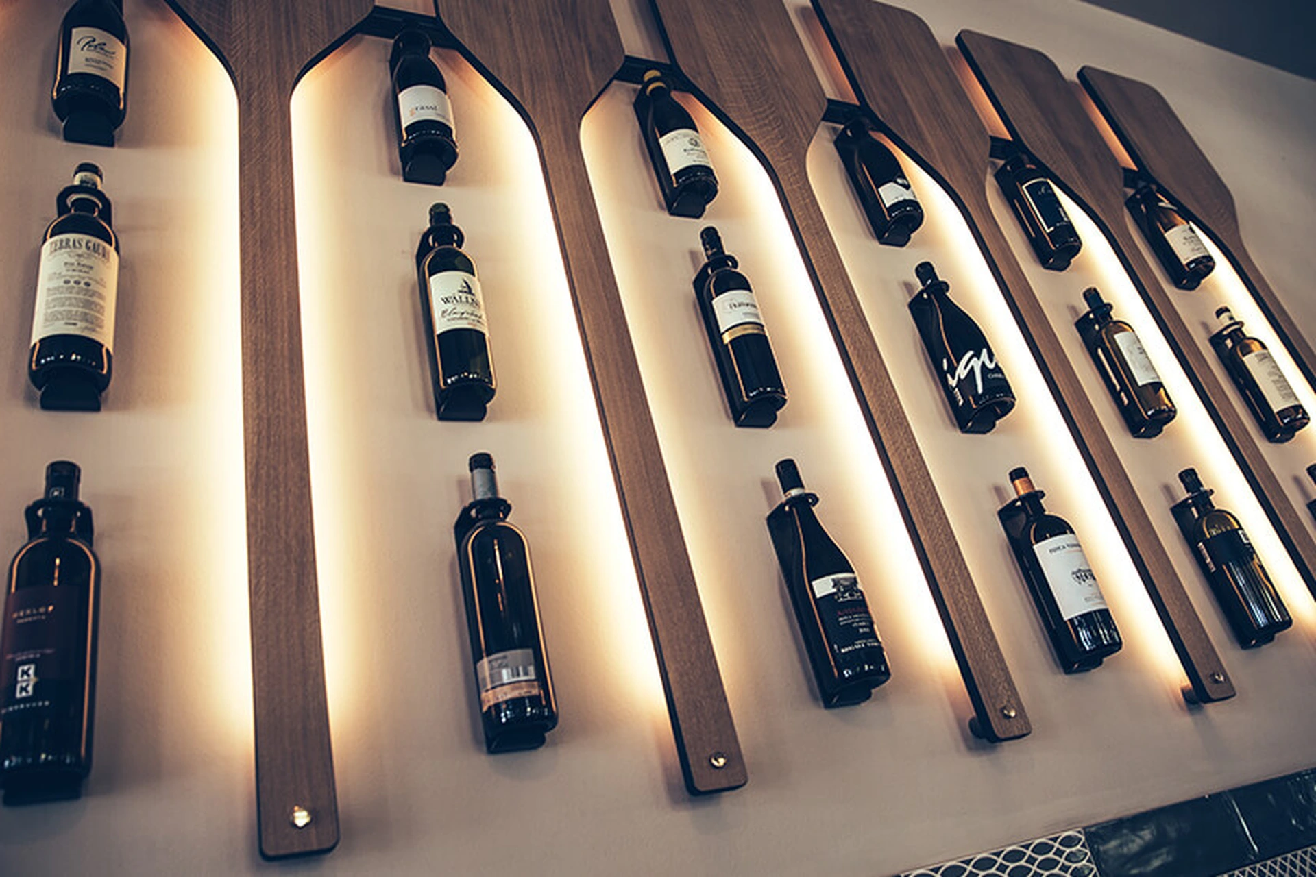 Detailaufnahme der hinterleuchteten Wanddekoration im Restaurant Pier 69 in Bregenz mit Weinflaschen, die auf stilisierten Holzrudern präsentiert werden.