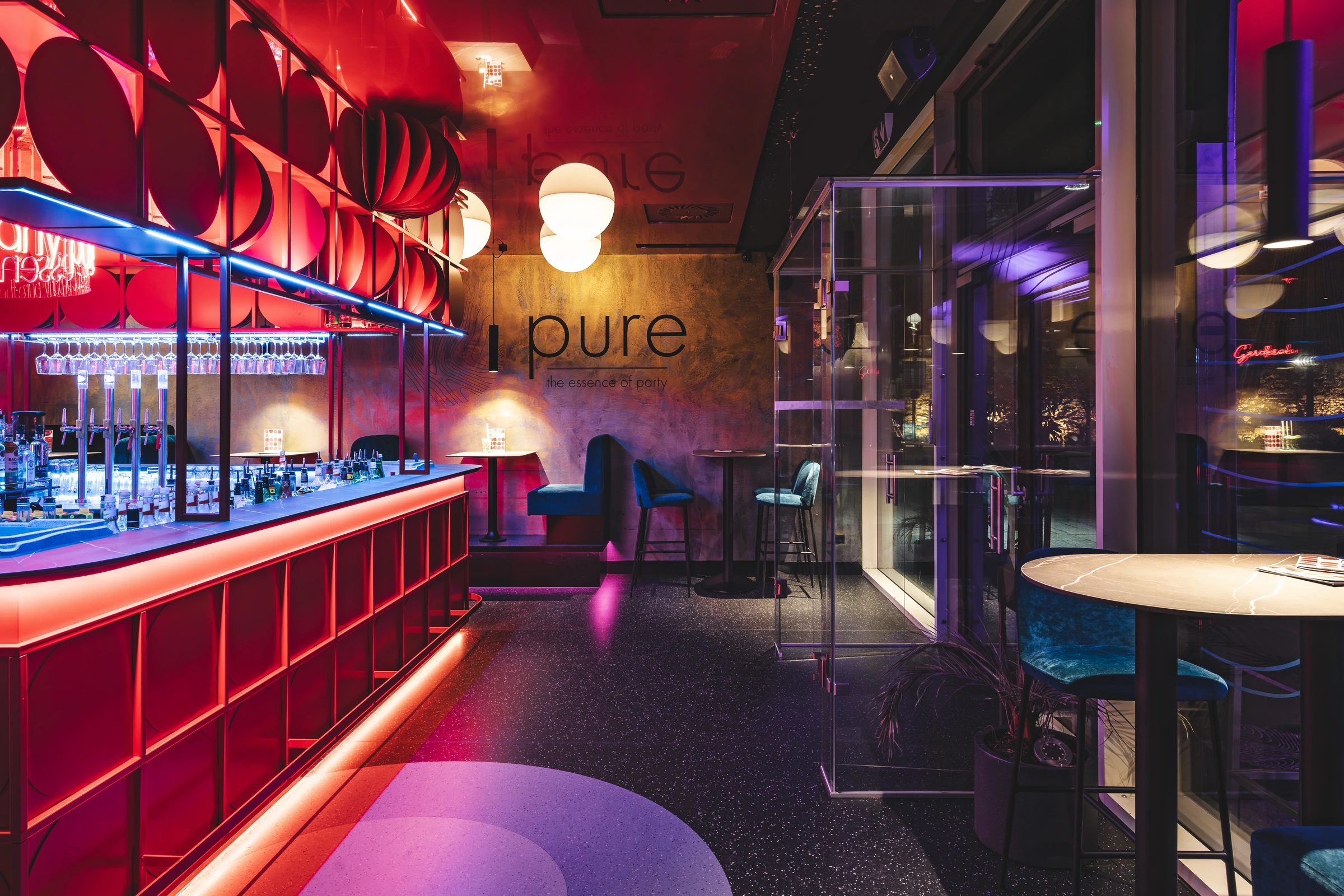 Gesamtansicht des Club Pure in Kufstein mit rot beleuchtetem Bartresen, markanter Wandinstallation aus roten Scheiben, „pure – the essence of party