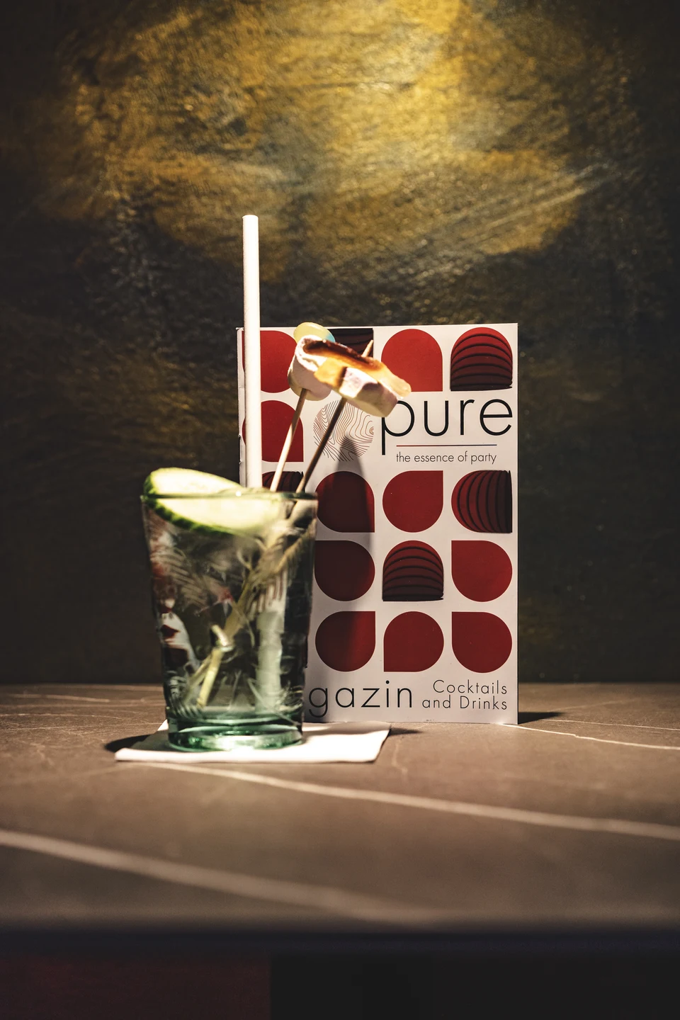 Cocktail mit Limette und Strohhalm neben der Getränkekarte des Club Pure in Kufstein mit dem markanten rot-weißen Design und dem Slogan „the essence of party