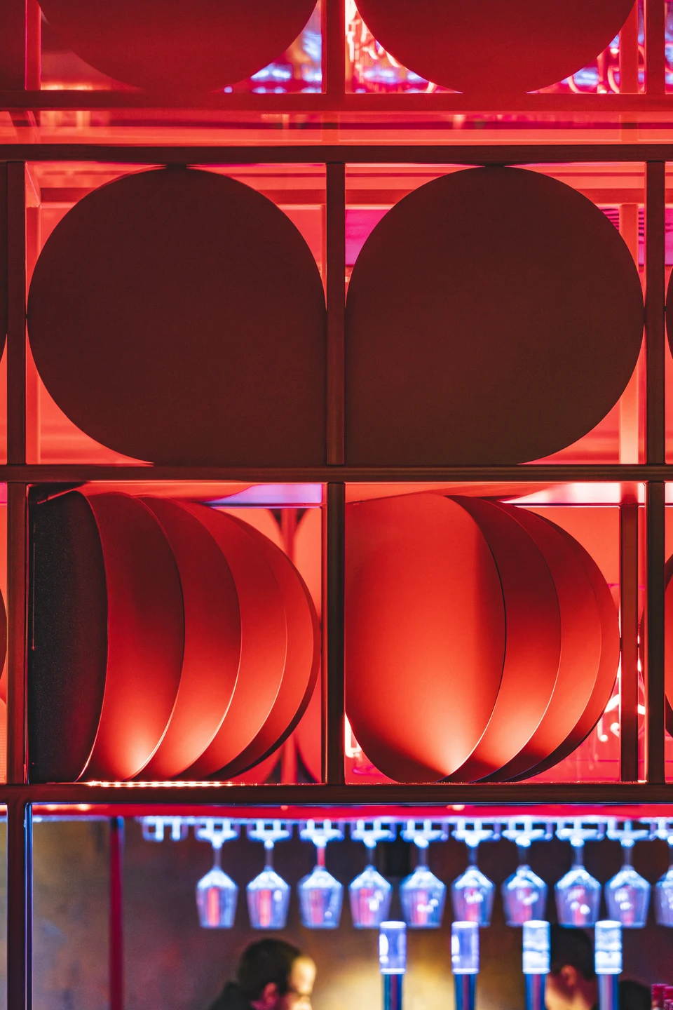Detailaufnahme der charakteristischen roten Scheiben-Installation über dem Bartresen des Club Pure in Kufstein, darunter hängende Weingläser in blauem Licht.