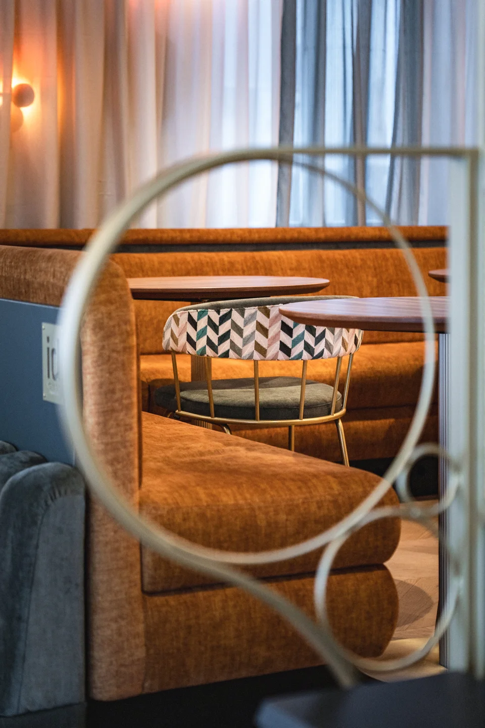 Detailblick durch goldene Ringelemente auf eine orangefarbene Samtbox mit gemustertem Barhocker und rundem Holztisch in der Bar Rio in Dornbirn.