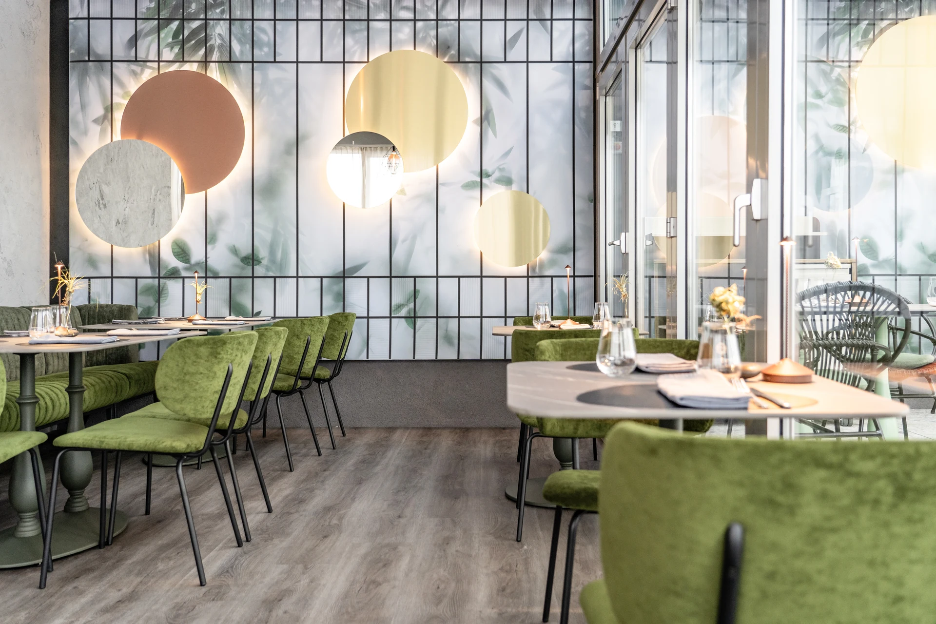 Gastraum des Restaurant Sam's in Eggelsberg mit grünen Samtsesseln, gedeckten Tischen, runden Wandspiegeln und Botanik-Tapete.
