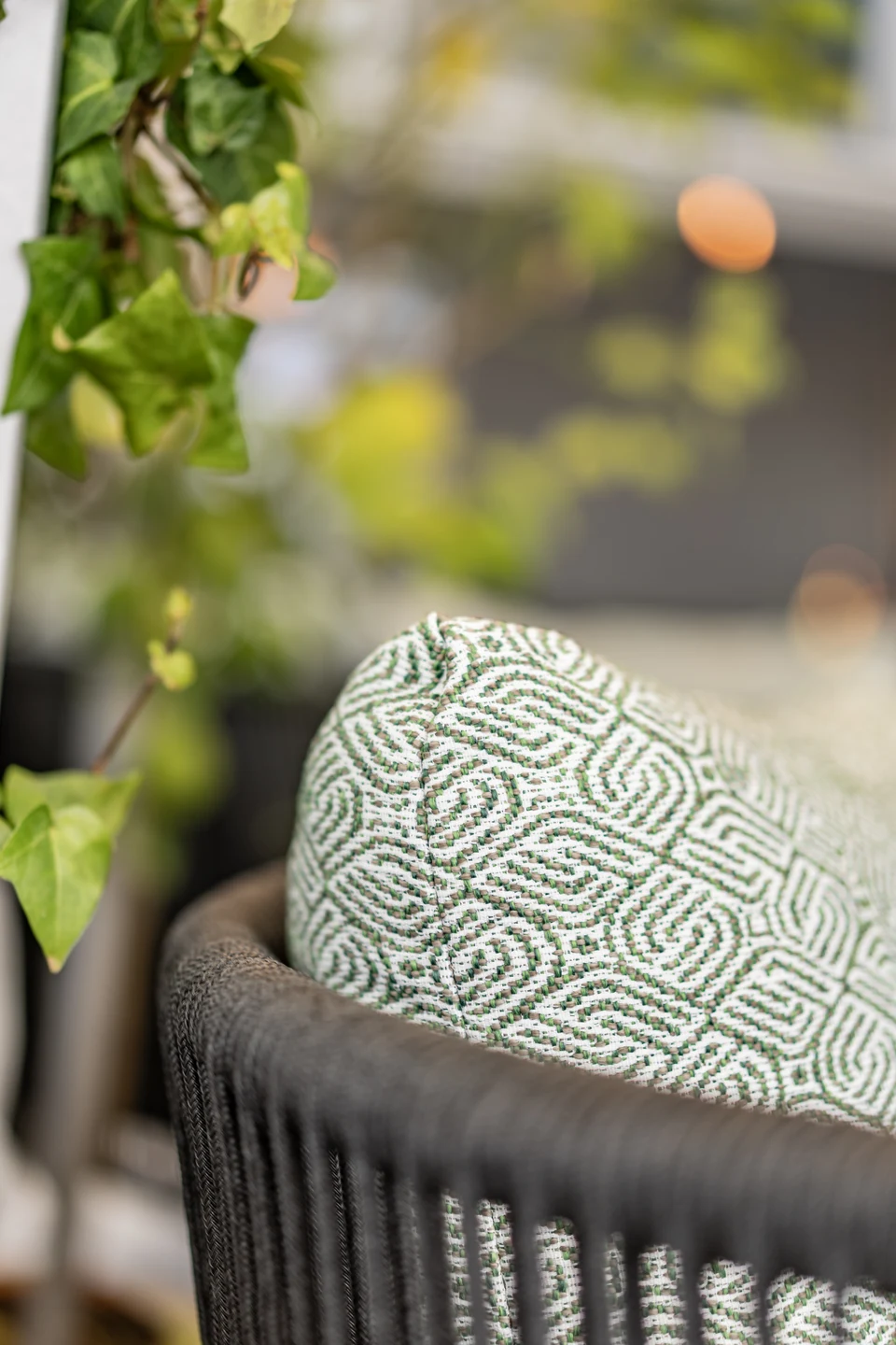 Detailaufnahme eines Korb-Outdoorsessels mit gemustertem grün-weißem Kissen auf der Terrasse des Restaurant Sam's in Eggelsberg, mit Efeu im Vordergrund.
