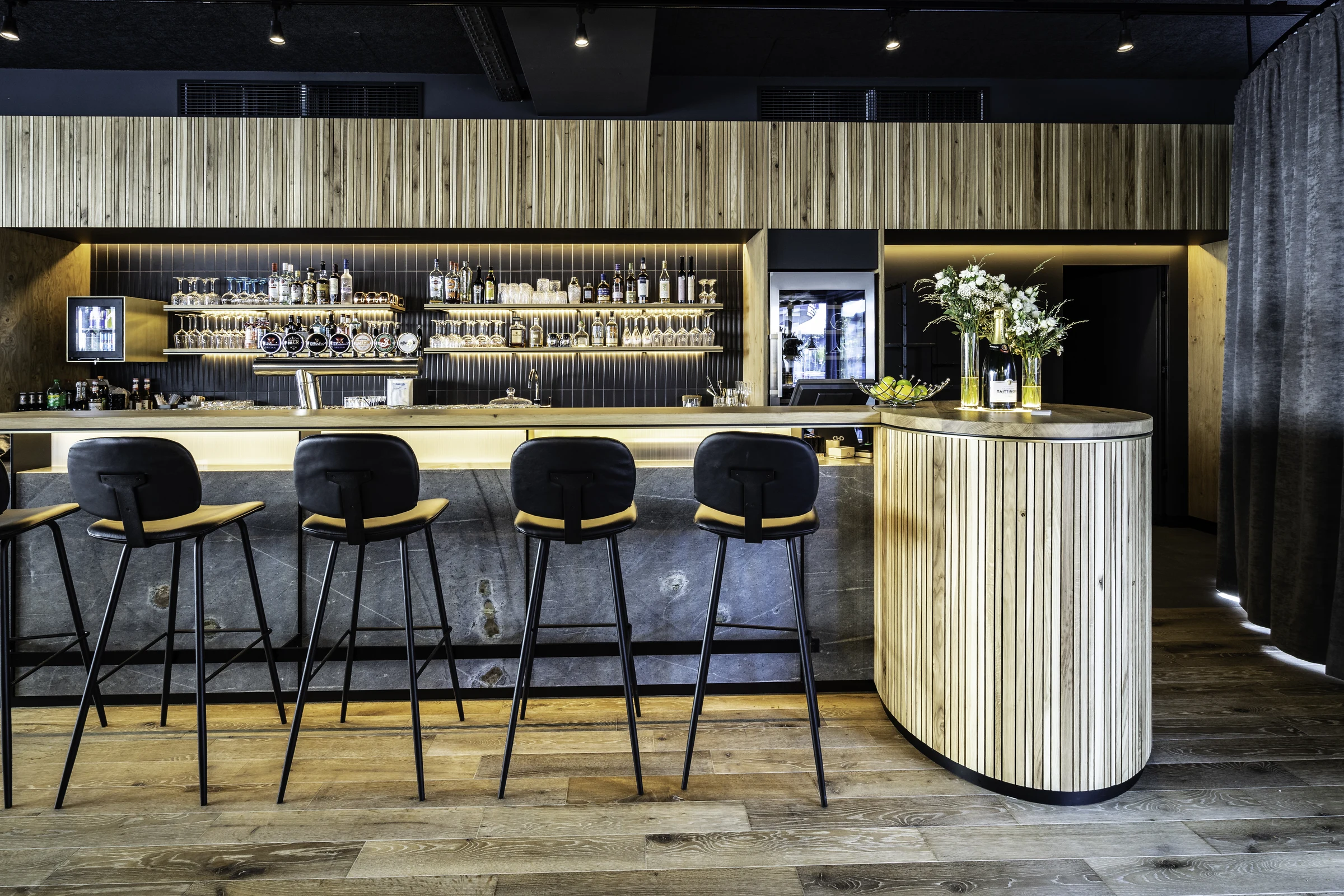 Bar des Restaurant Scanaua in Schaan mit schwarzen Barhockern, beleuchtetem Spirituosenregal und Holzlamellen-Verkleidung.