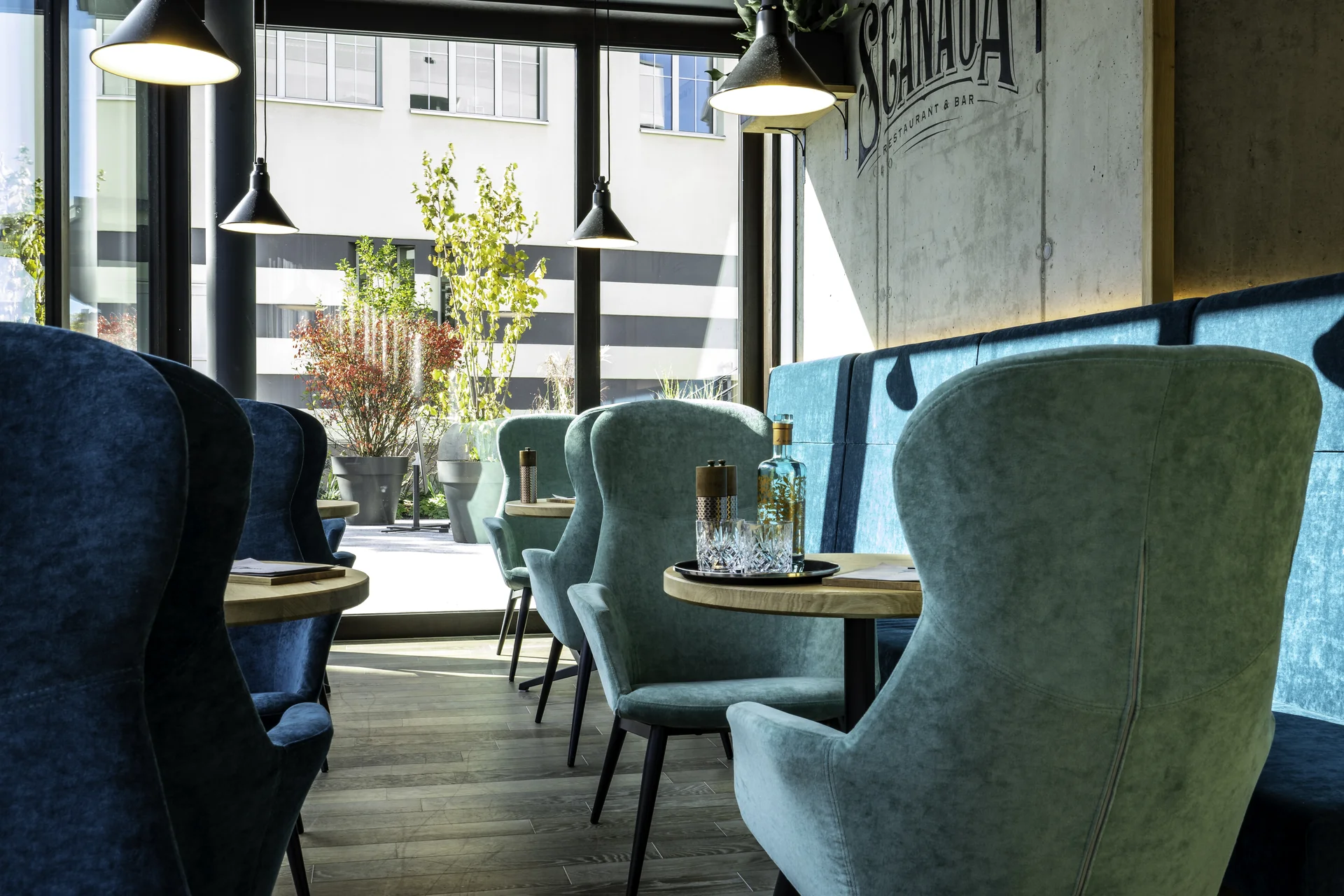 Lounge-Bereich des Scanaua in Schaan mit blauen und türkisen Ohrensseln, Logoschriftzug und Panoramafenster zum Innenhof.