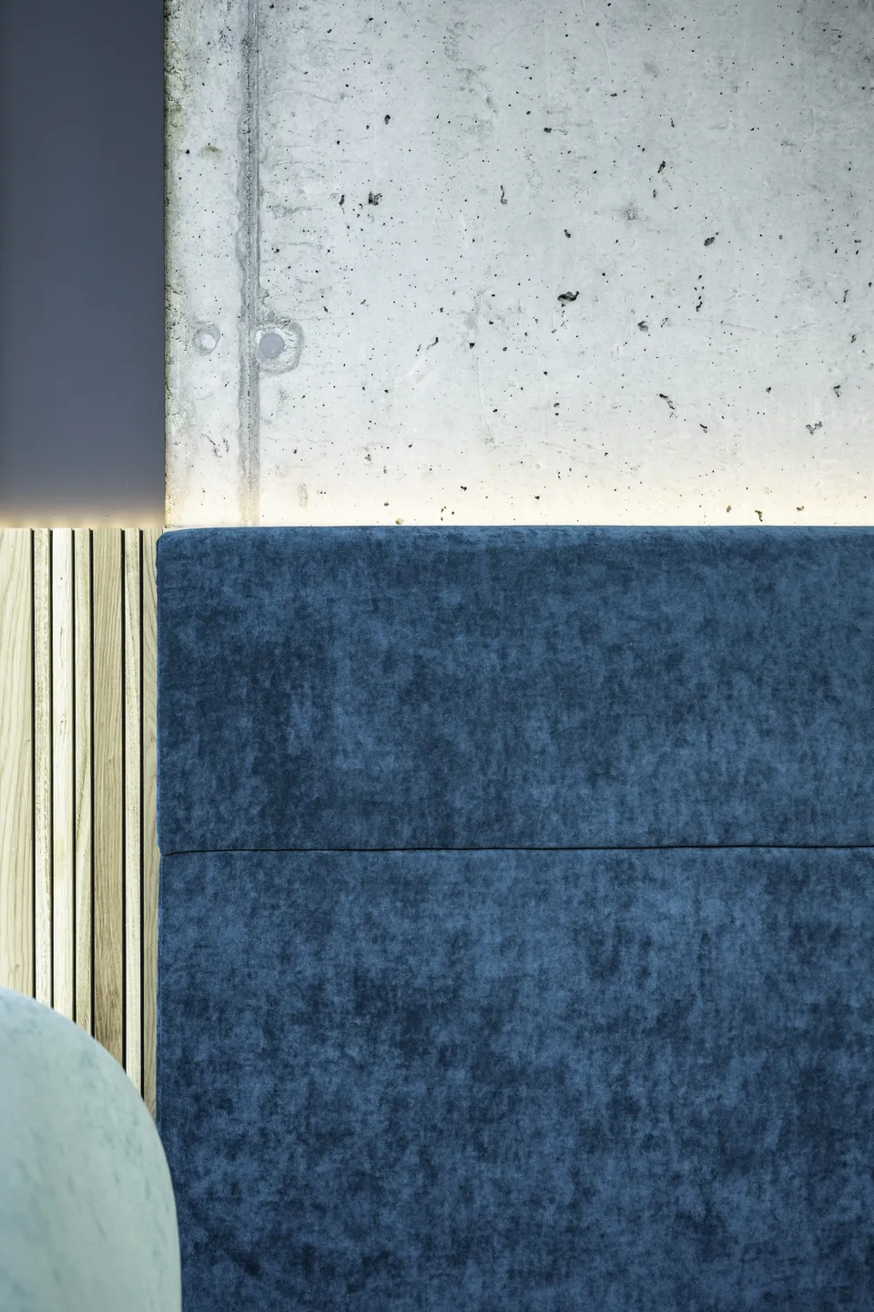 Detailaufnahme einer blauen Samtbank vor Sichtbetonwand mit Holzlamellen und indirekter Beleuchtung im Scanaua Schaan.