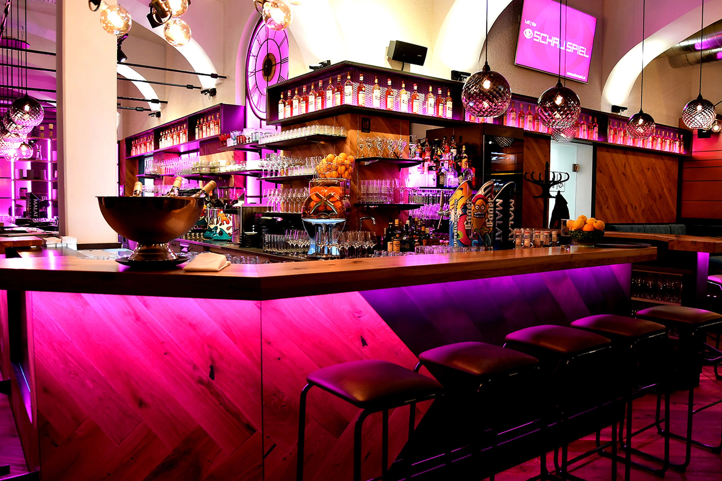 Bar des Schauspiel mit pinker Ambientbeleuchtung, Barhockern, beleuchtetem Spirituosenregal und Gewölbedecke.