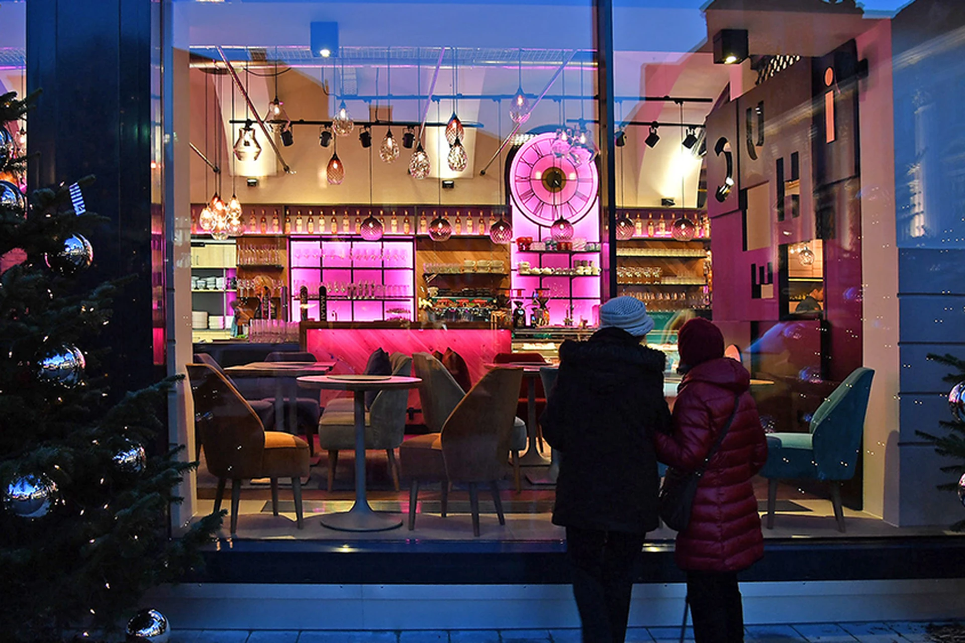 Außenansicht des Schauspiel bei Nacht durch die Schaufensterfront mit pinker Barbeleuchtung und Weihnachtsbäumen.