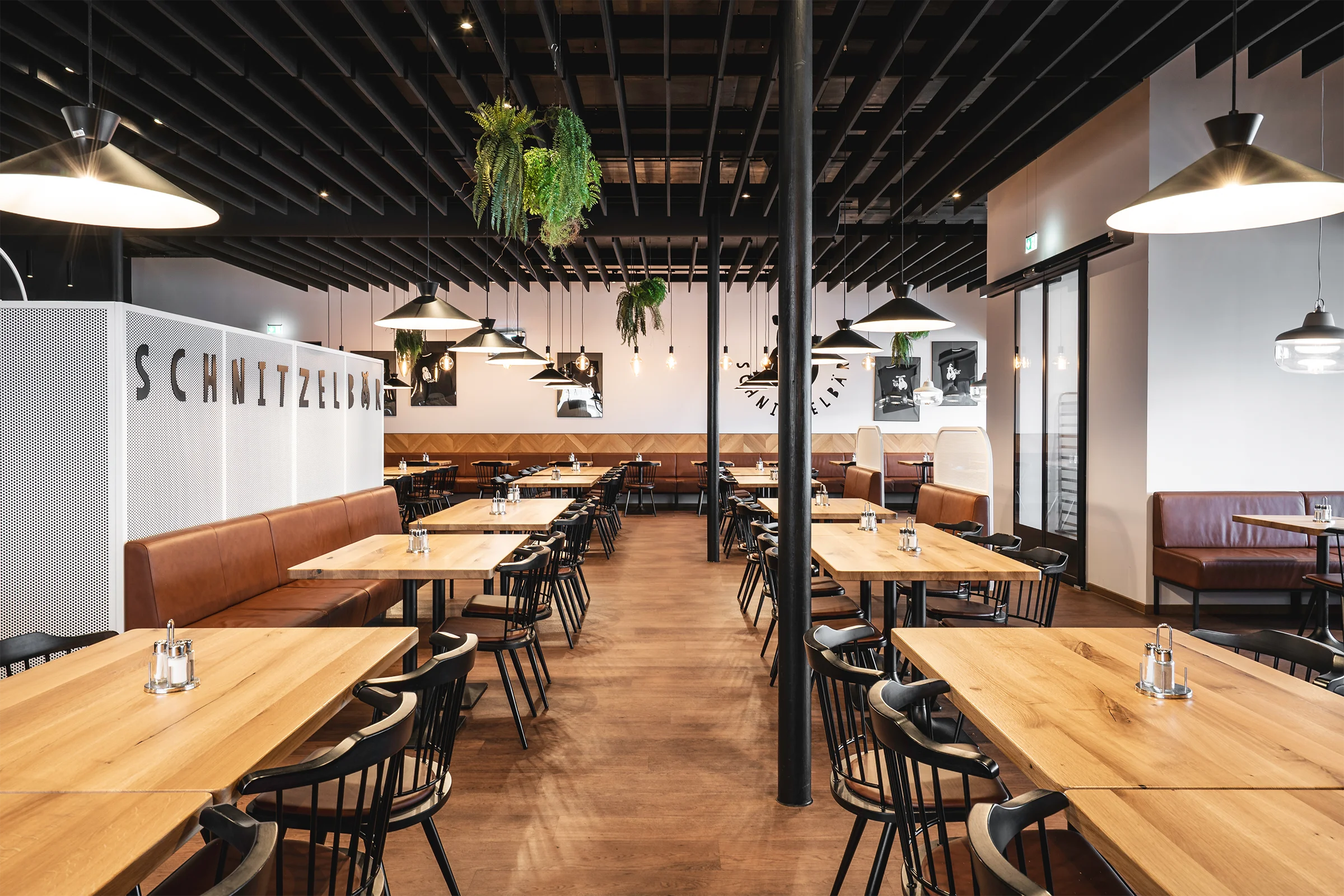 Gesamtansicht eines SB Schnitzel Restaurants mit großzügigem Sitzbereich, Akustikpaneelen, Hängelampen mit Dekoschirm und modernem Raumkonzept