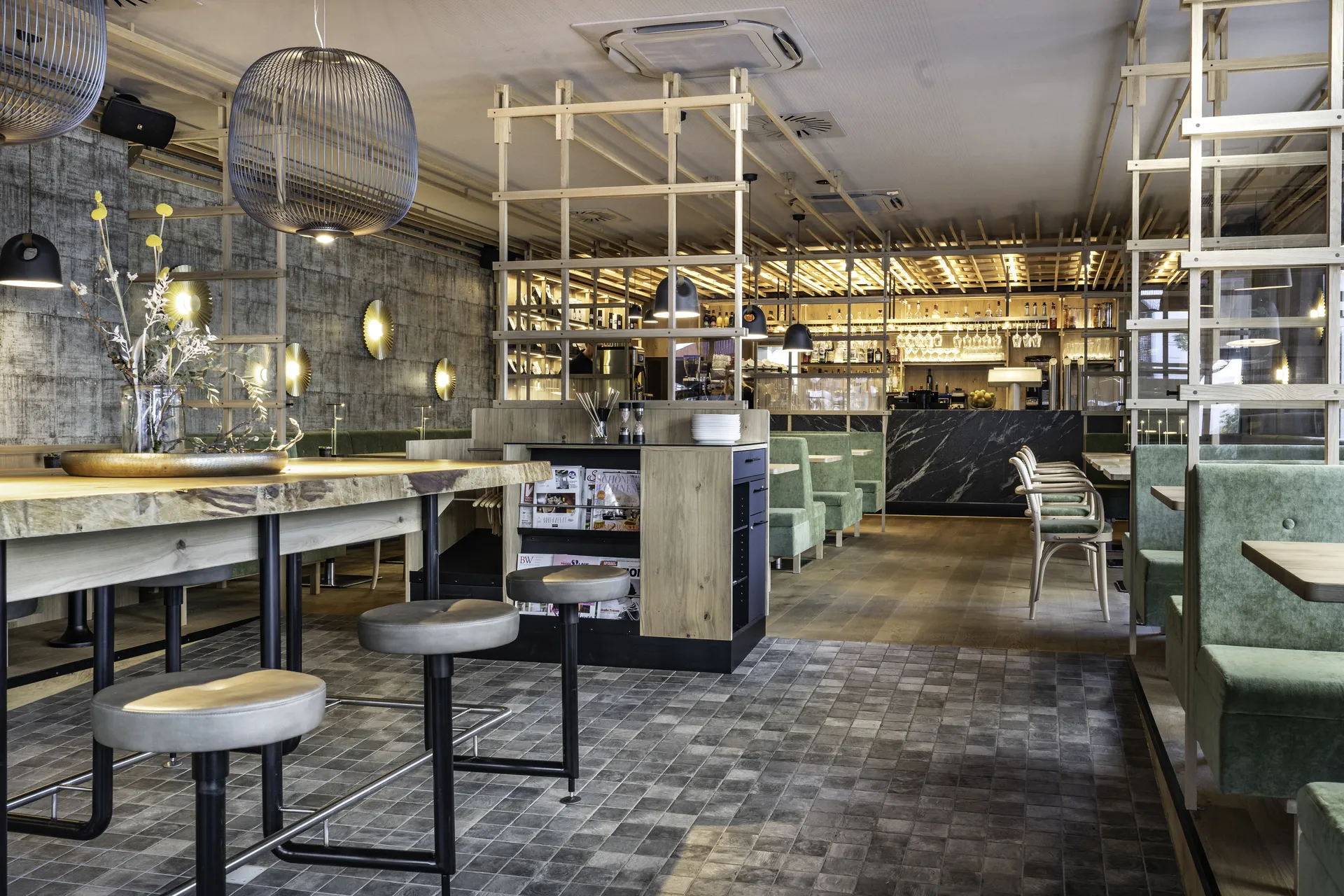 Gastraum des Café 21 in Dornbirn mit Stehtisch, Hockern, grünen Samtbänken, schwarzem Marmortresen, Zeitschriftenständer und Gitter-Pendelleuchte.