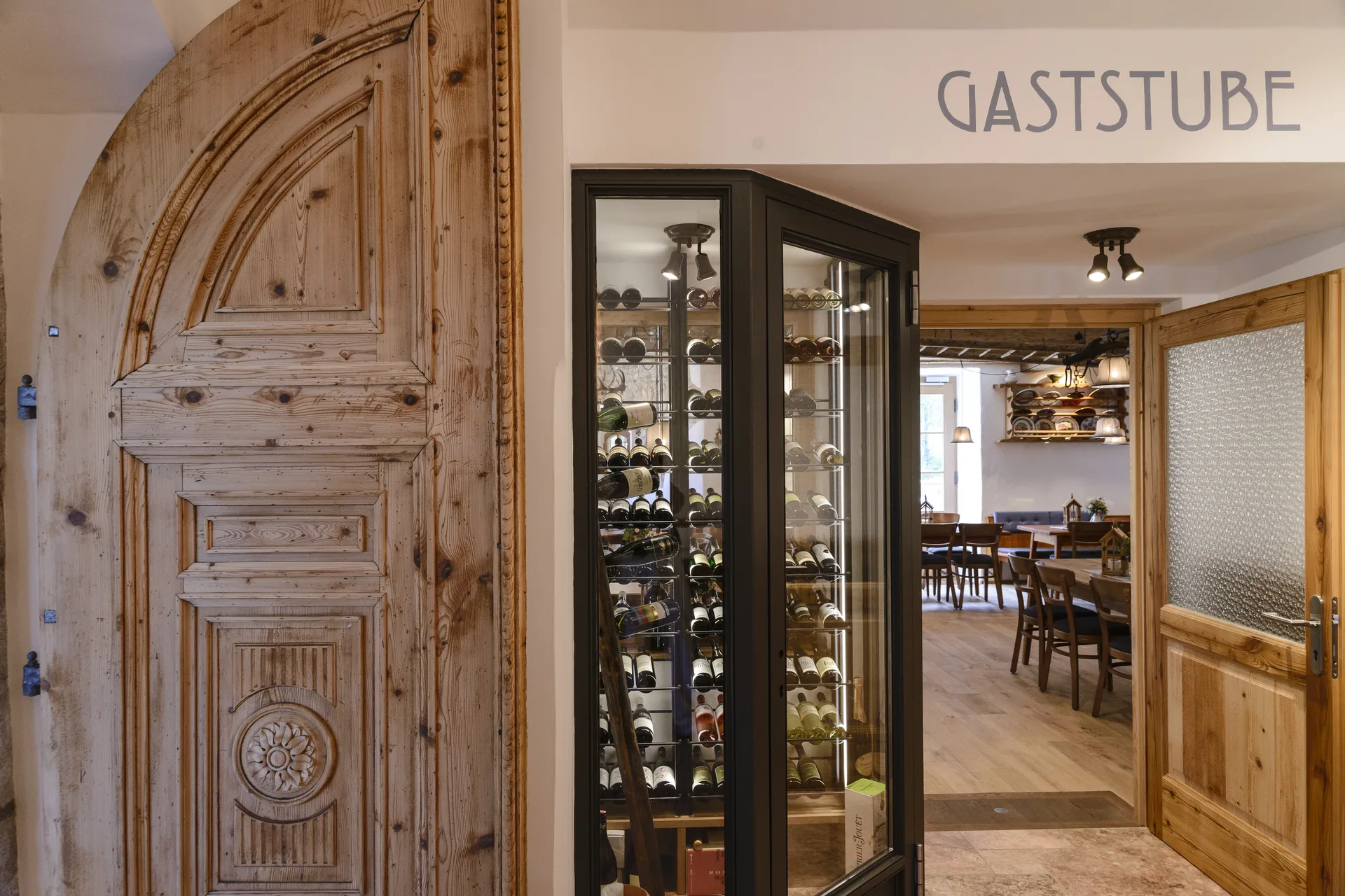 Eingangsbereich zur Gaststube des Steegwirt in Bad Goisern mit historischer Holztür im Steinrundbogen und beleuchtetem Weinkühlschrank mit Weinflaschen.