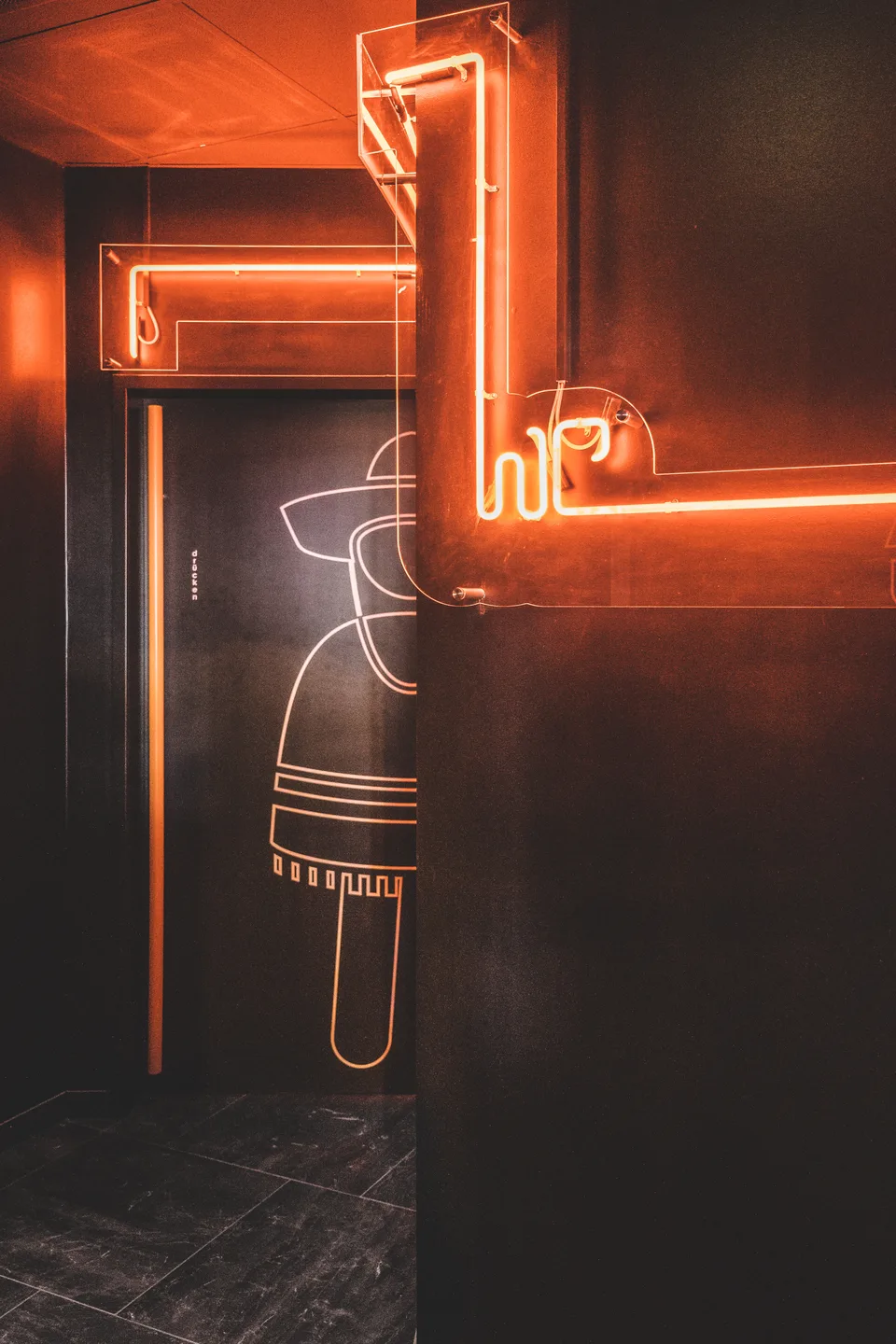 WC-Bereich des Taco Taco in Lustenau mit orangem Neonschriftzug, Taco-Wandzeichnung auf schwarzer Wand und stimmungsvoller Ambientbeleuchtung.