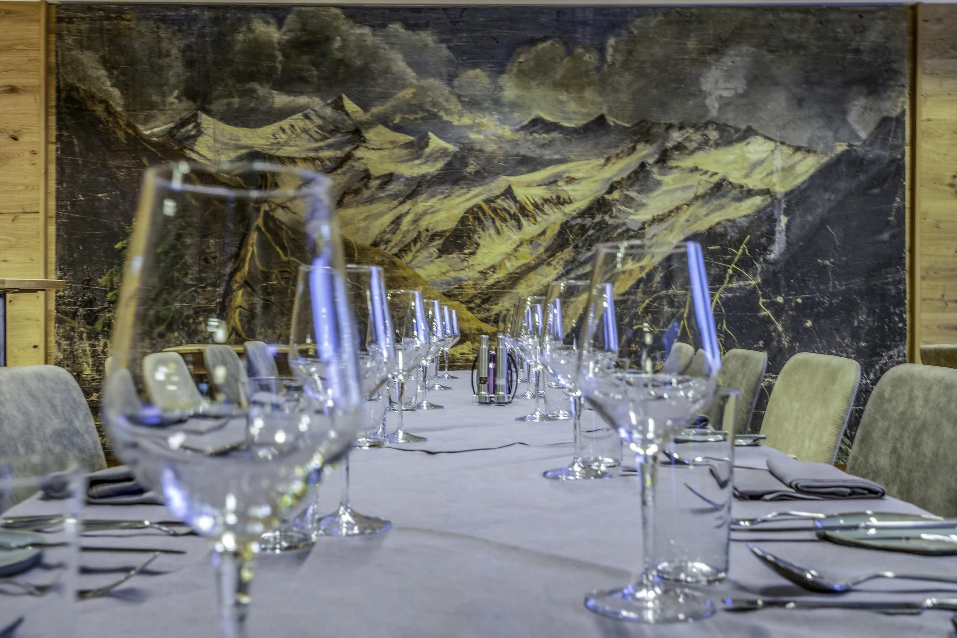 Private-Dining-Bereich der Venediger Lodge Neunkirchen mit langem gedeckten Tisch, Weingläsern, lila Servietten und großem Ölgemälde einer Berglandschaft als Wandbild im Hintergrund.