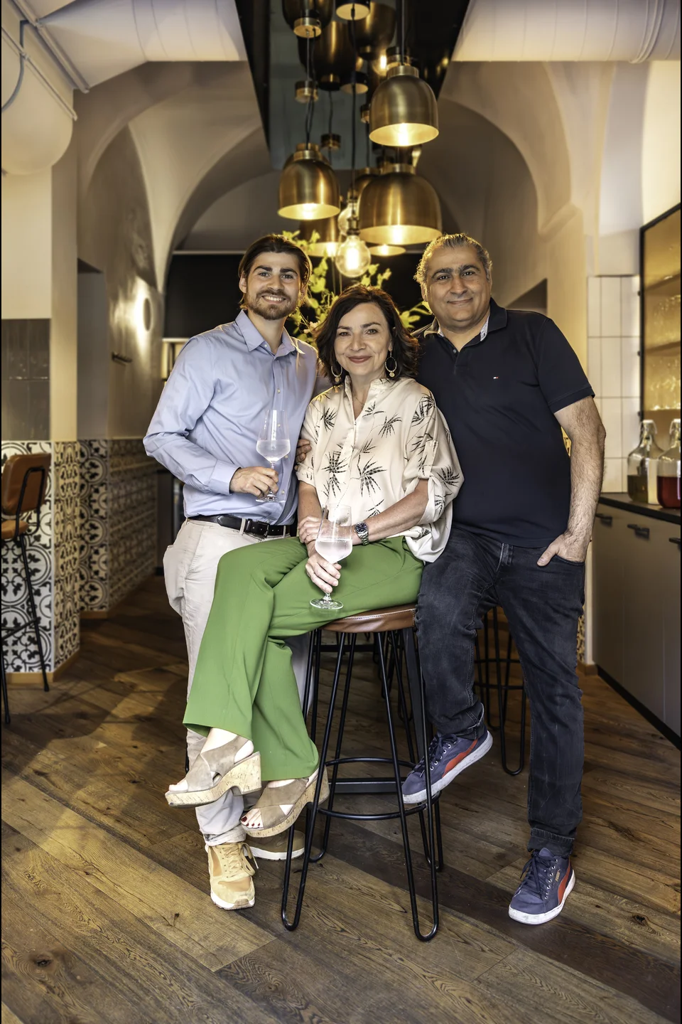 Das Team des Wirt am Platzl Garsten – zwei Männer und eine Frau mit Weingläsern – posiert in der Weinbar vor marokkanischen Wandfliesen, Messingglockenleuchten und historischem Gewölbe.