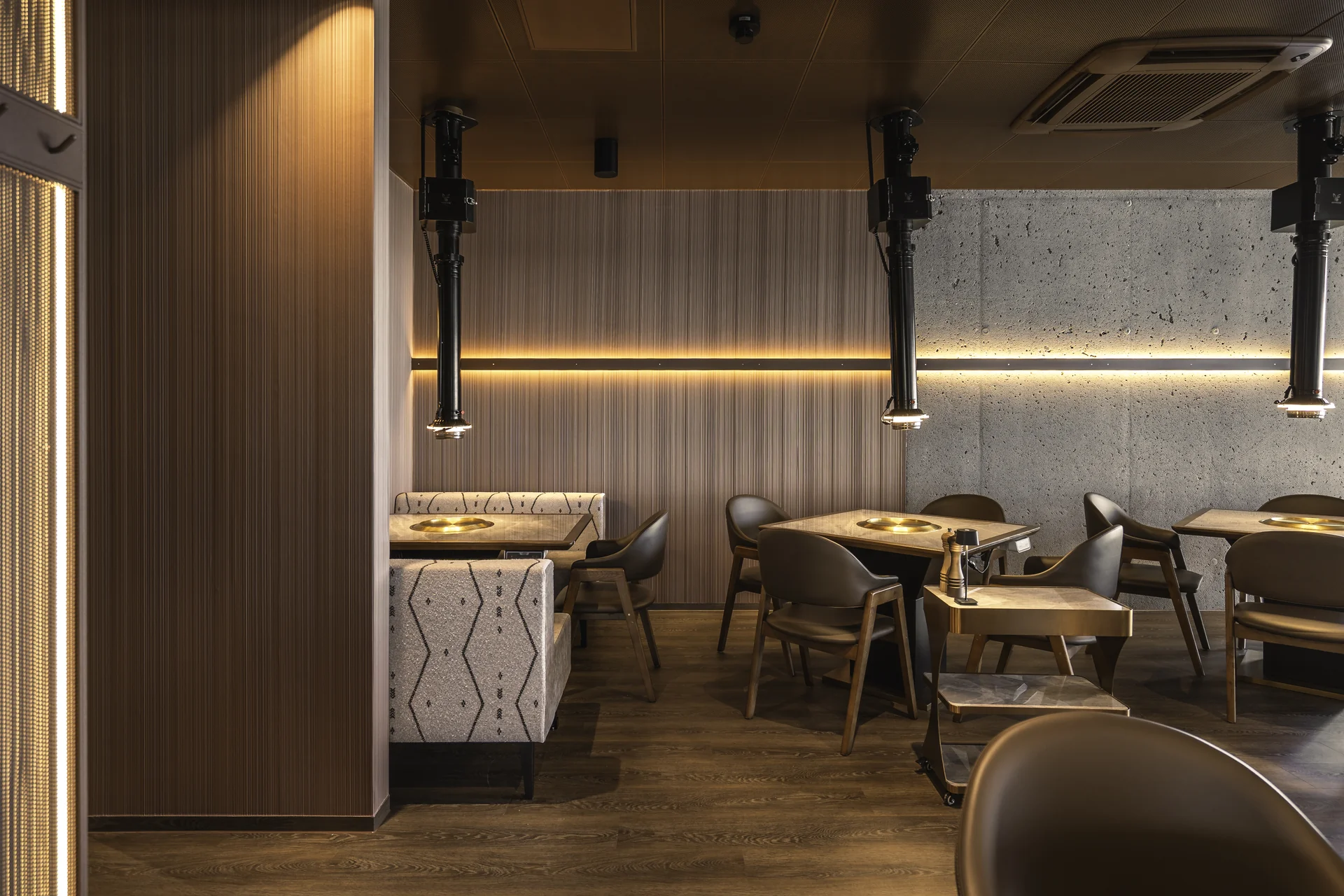 Sitzbereich mit Grilltischen, Sichtbeton und goldenem Lichtband im Restaurant Akiko.