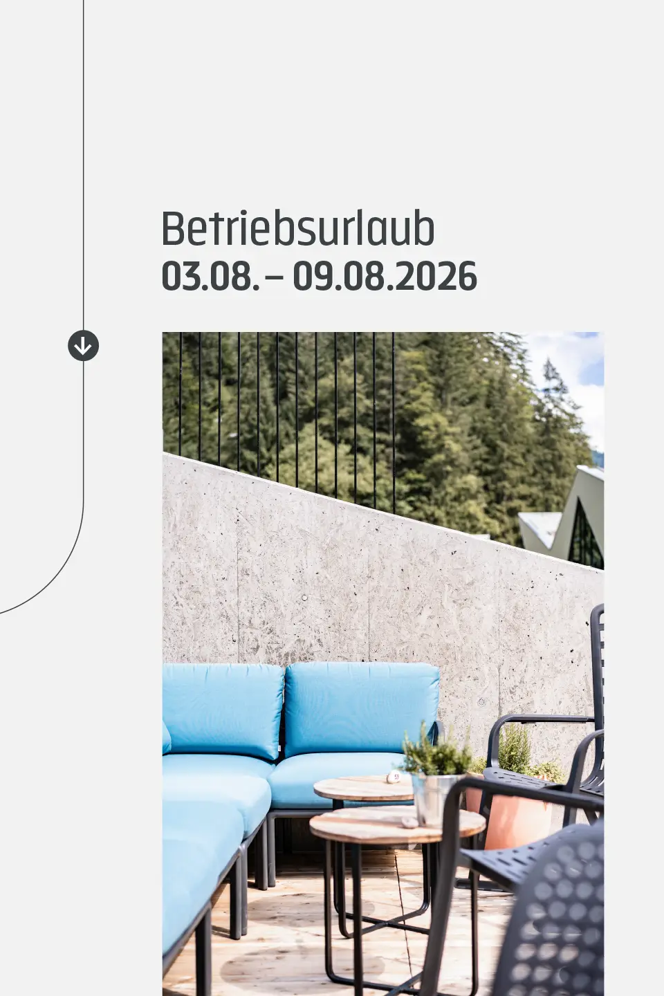 Terrasse mit blauen Loungemöbeln vor Betonwand und Bergpanorama, Ankündigung Betriebsurlaub id-werkstatt