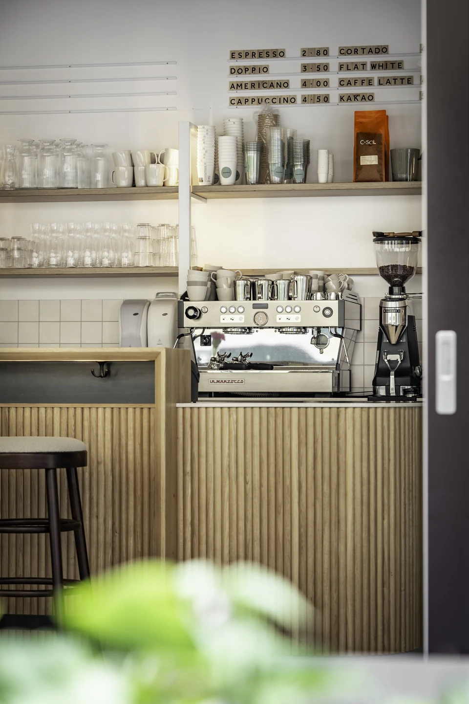 Kaffeestation der Almgreißlerei Salzburg mit professioneller Espressomaschine, Glasregalen und handgeschriebener Getränketafel.