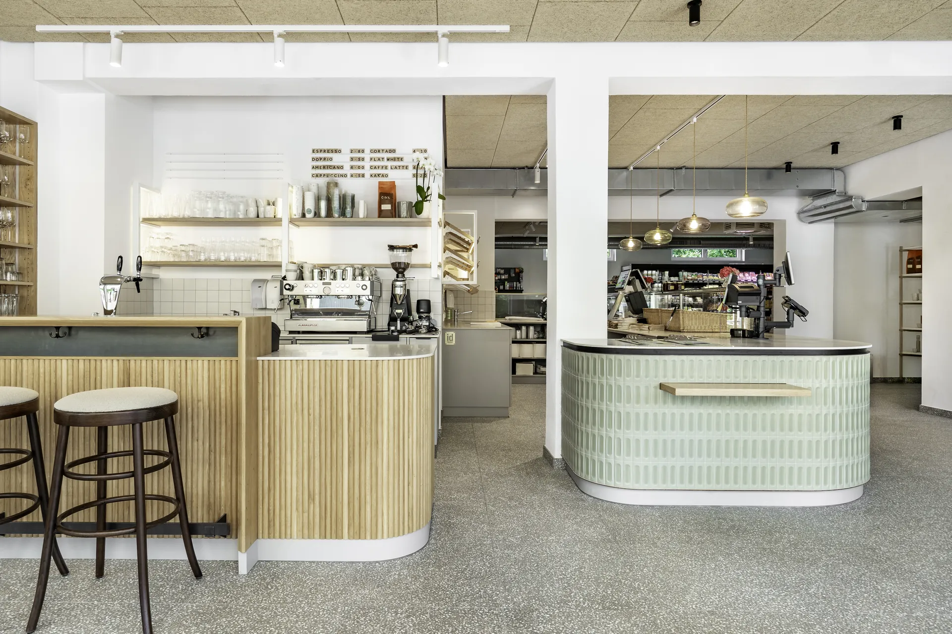 Übersicht des Gastraums der Almgreißlerei Salzburg mit Holz-Kaffeebar, rundem grünen Kassentresen und Terrazzoboden.