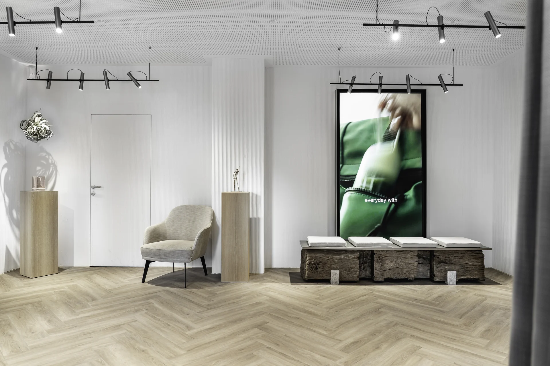 Wartebereich der Biogena Plaza Wien mit Sessel, Holzsockeln, silberner Skulptur und grünem Digitalscreen im Hintergrund.