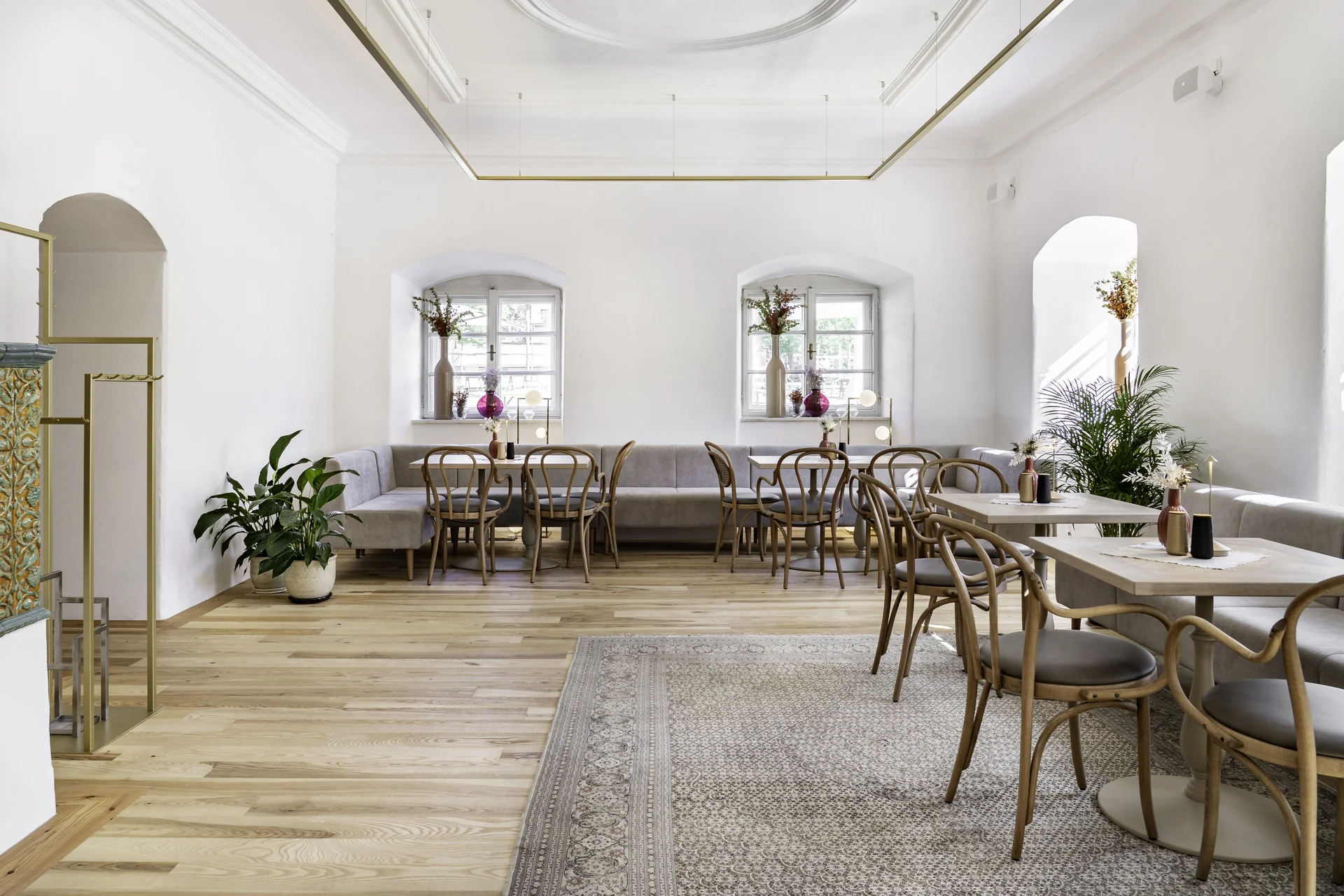 Weißer Saal der Fiegnerin im Schloss Fügen mit Stuckdecke, Messingrahmen, umlaufenden Sitzbänken, Bugholzstühlen und Vintage-Teppich.