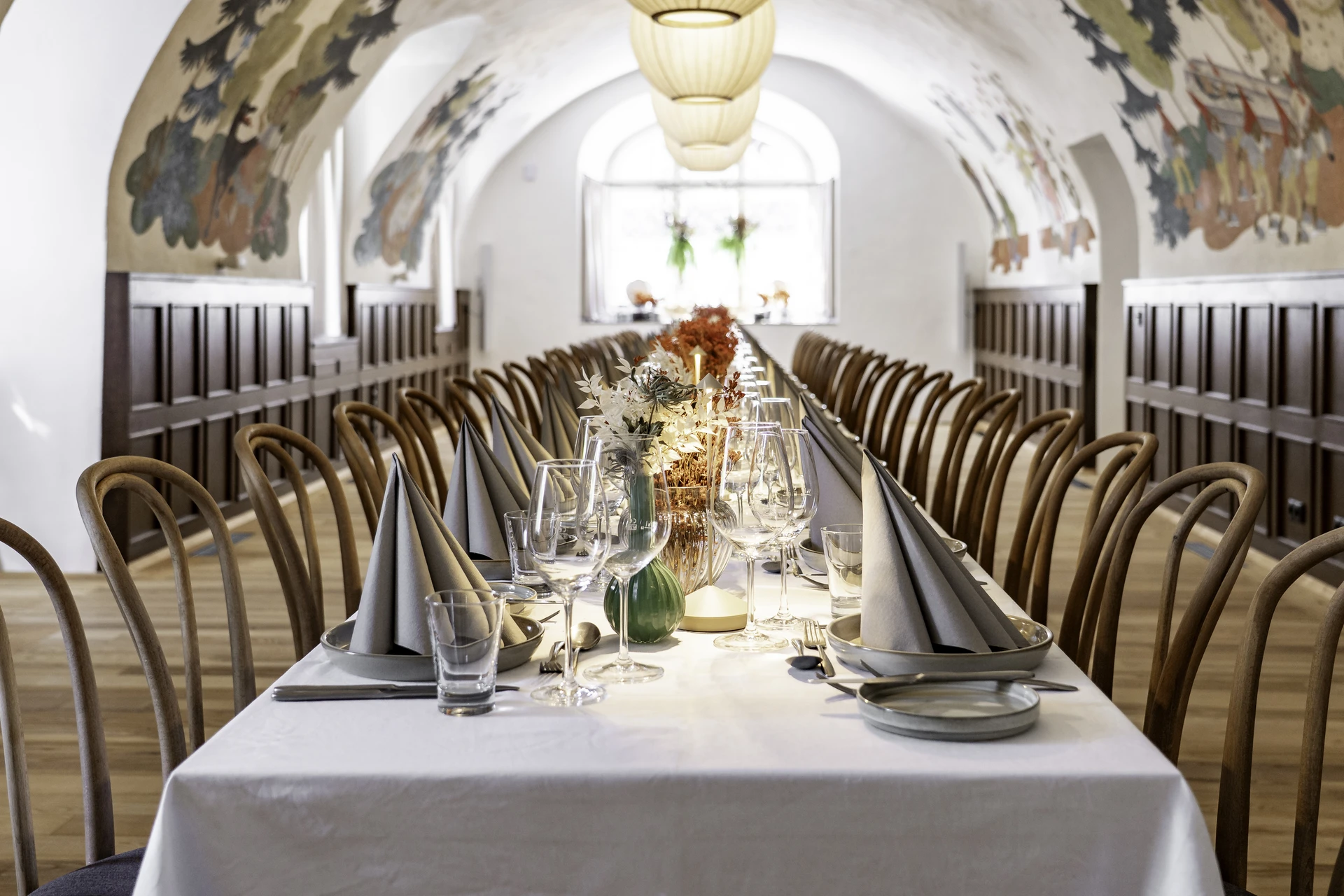 Märchensaal im Schloss Fügen mit bemaltem Tonnengewölbe, dunkler Holzvertäfelung, Papierleuchten und langer, festlich gedeckter Tafel mit Bugholzstühlen.