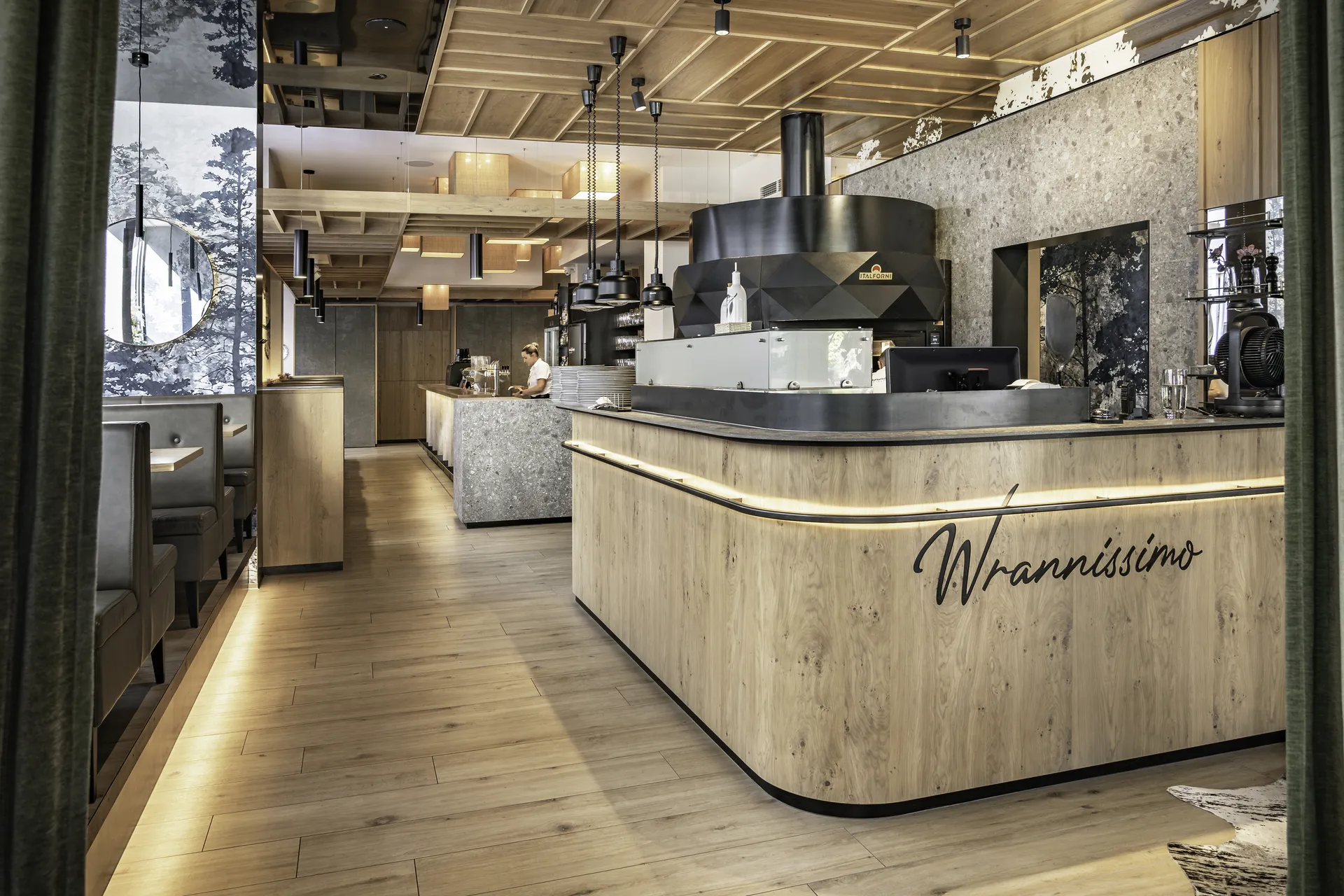 Pizzastation im Wrannissimo in Velden mit hinterleuchtetem Holztresen, Wrannissimo-Schriftzug, schwarzem Dunstabzug und Terrazzowand.
